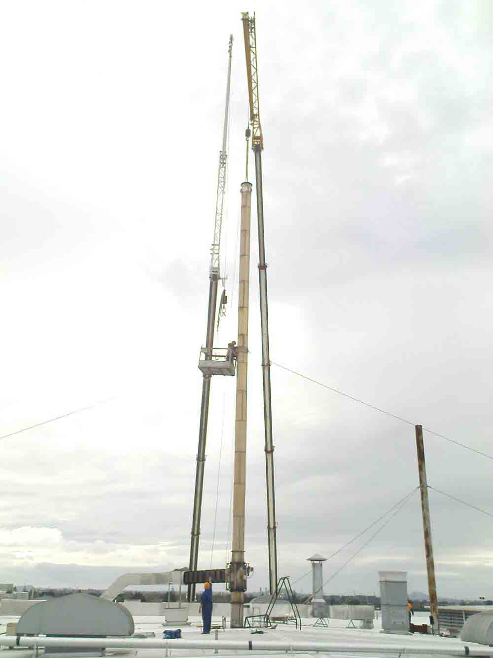 Tall industrial stack being installed by crane on a factory roof